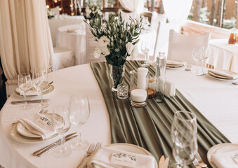 glass vase with a bouquet of white flowers in the middle of the served festive table. olive colore drapery on a white set table