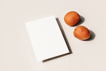 Summer still life composition. Fresh orange apricot fruit and on beige table background. Blank paper greeting card, invitation mock up scene. Birthday party concept. Simple design, no people.
