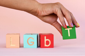 A woman's hand with rainbow nails lays out the inscription LGBT from cubes. abbreviation LGBT on a pink background.