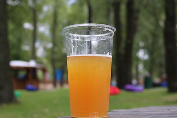 
A plastic glass with beer stands on a wooden table in nature