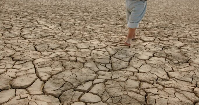 Close up shot of legs of baby boy running on cracked soil, destroyed by overuse, climate change and flood - ecological issues, save our planet 4k footage
