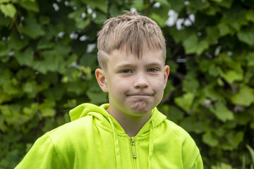 Street portrait of a 10-year-old boy with a grimace on his face against the background of nature. Concept: soon to school, summer vacation in the country.