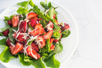 Summer salad with strawberries on a white plate and a light background. Close up. Place for copy space