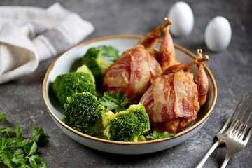 Baked quail in bacon with boiled broccoli and olive oil.