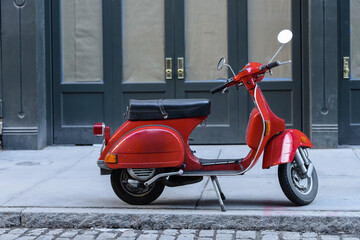 Red, small motorbike on the sidewalk in a city.