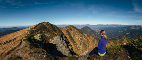 Female hiker sitting on the top of the mountain and enjoys breathtaking panoramic view.