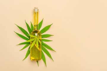 Medicinal cannabis with extract oil in a bottle and hemp leaf on camel color background. Medical cannabis concept.