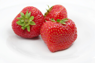 Three red ripe strawberries on a white plate. Strawberries isolated on a white background.