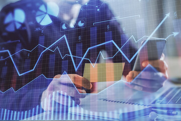 Double exposure of man's hands holding and using a phone and financial graph drawing. Analysis concept.