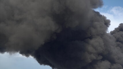 Black smoke rises above the buildings. A big chemical fire at a factory building. Thick black smoke covers the sky.
