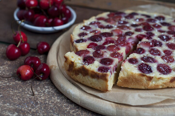 Tart with ripe sweet cherries on wooden circle board on brown background. Homemade dessert with ripe sweet cherries. 