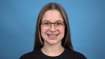 Teen girl with braces smiling on a blue background. Girl with colored braces.