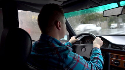 A young man is driving a car. Rainy weather. A view of a man from behind from the back seat