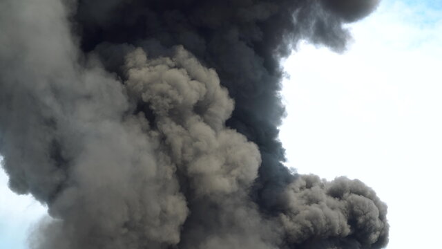 Black smoke rises into the sky. A big chemical fire at a factory building. Thick black smoke covers the sky.