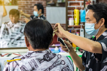 The hairdresser is doing hairdressing for an elderly Thai man.