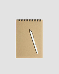 Blank spiral notepad mockup template with kraft paper cover with  white glossy pen isolated on light gray background.