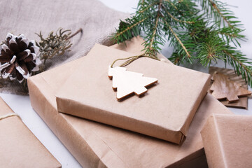 gift box wrapped in eco paper and decorated with a wooden Christmas tree figurine, natural spruce branches and pine cones for decorating gifts in eco style