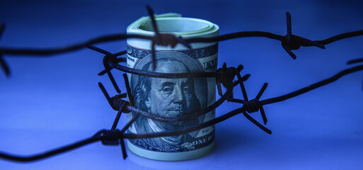 Barbed wire against US Dollar bill. Economic warfare, sanctions and embargo busting.