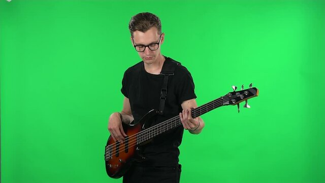 Portrait professional musician playing the electric guitar. Young guy with glasses and a black T shirt on a green screen in the studio.
