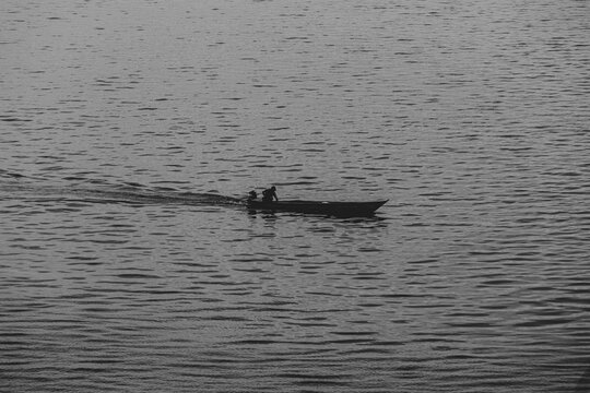 Panoramic view of a small fishing boat floating and moving on Rio Negro in Amazonia. Black and white concept.