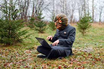 Halloween Scarecrow with a carved pumpkin on its head is fiercely typing a message on a laptop keyboard