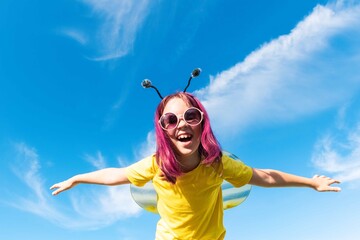 Girl in a bee costume with pink hair outdoors. Looks into the camera