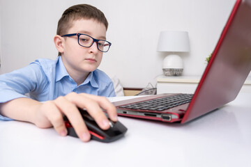 A school boy sitting by the table with a laptop and doing homework, e-learning, online education and home school concept
