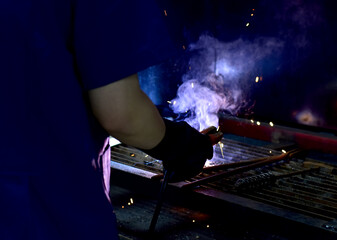 Thai Technologist Steel welding metal In the workshop class with flames and smoke floating out.