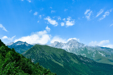 Fototapeta premium A beautiful view of the snow-capped mountain peaks of the Caucasus Mountains. White clouds against the blue blue sky.