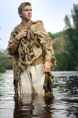 medieval peasant in a ragged raincoat of old sacking wades through the river
