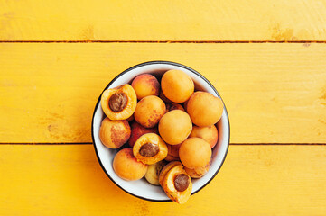 ripe juicy homemade apricots with cracks and flaws in the plate and scattered on a bright yellow wooden surface. Harvest 2020