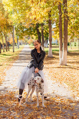 Obraz premium Ballerina with Dalmatian dog in the Park. Woman ballerina in a white ballet skirt and black leather jacket dancing in pointe shoes in autumn park with her spotty dalmatian dog.