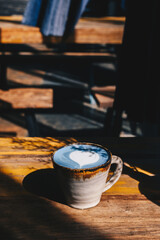 A cup of Blue latte on wooden table. The vibrant blue colour of the drink is natural, Made from micro-milled Butterfly Pea Flower, which originated in Thailand.