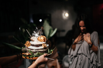 Portrait of charming girl blowing on candles on birthday cake surrounded by friends at party