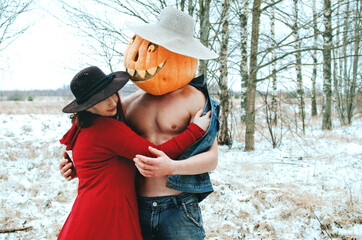 witch and a Halloween Scarecrow with a carved pumpkin on their head are embracing in a field, it...