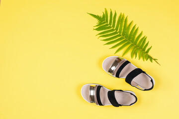 Top view of black and white sandals and a palm leaf on a yellow background.