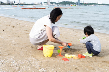 Mother and 3 years old asian kid play sand on the beach. Background for family life and education. holiday with children.