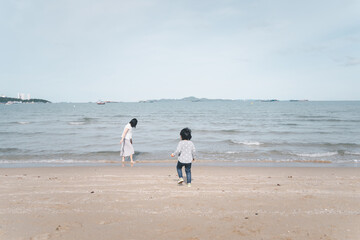 Mother and 3 years old asian kid walking on the beach. Background for family vacation and recreation.