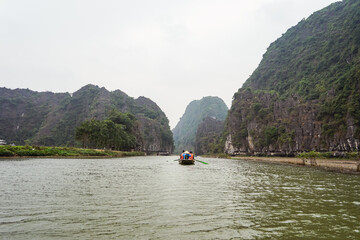 unrecognizable tourists visiting Tam Coc in rowboat along river with beautiful landscape of karst mountains