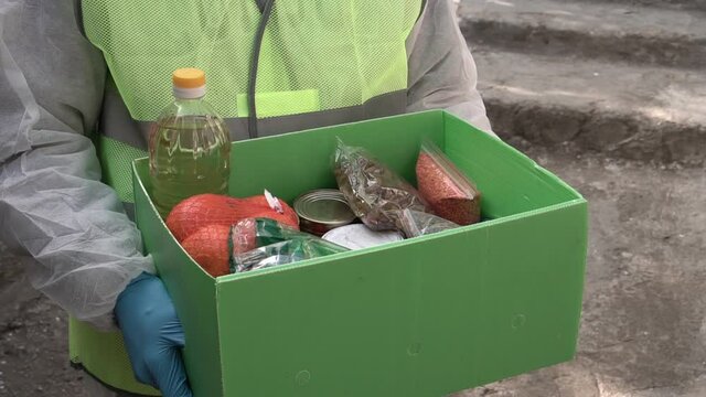 Volunteers In The Protective Mask And Hand Gloves Distributes Charity Boxes. Delivery Meals To Senior, Family In Need. Food Bank During COVID-19. Volunteering Fund, Charity And Donation, Food Parcel 