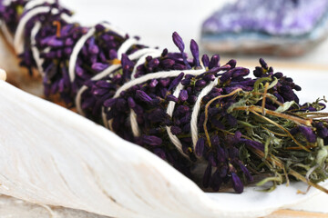A close up image of a healing smudge stick with lilac flowers and amethyst crystal. 