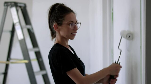 Atractive woman paints bedroom with paint roller - side profile medium shot