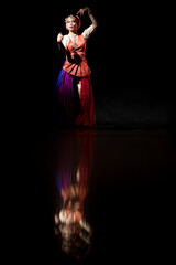 Transgender Asian person doing traditional Indian dance in front of a dark black background. Dressed up like an Indian Goddess.