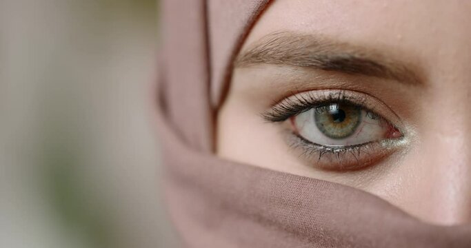 Face of muslim girl wearing traditional hijab head scarf and makep. Her eye with brown and green iris sensually looking at camera - beauty concept extreme close up shot 4k footage