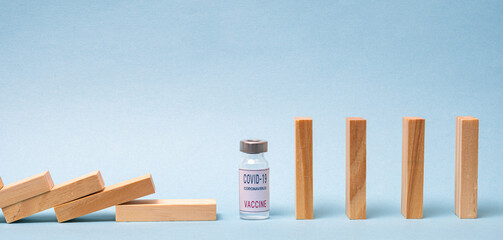 Vaccine concept with wood domino and COVID-19 vaccine ampoule on blue background.