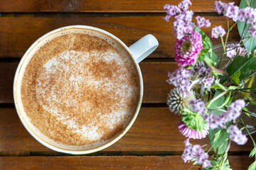 A cup of coffee with milk and a beautiful lilac-hued flowers, view from above
