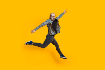 Fototapeta na wymiar Jumping caucasian man with blonde hair and eyeglasses is listening to music on yellow studio wall