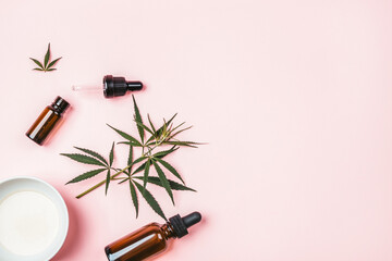 Cannabis leaf, hemp oil bottle and cup with oil on a pink background.
