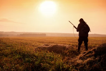  Hunter on the background of the sunset are on the field. Hunter In Sunrise With Shotgun in Autumn Season. © Sergey