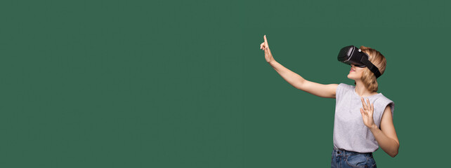Lovely young blonde woman with vr headset touching something on the green studio free space